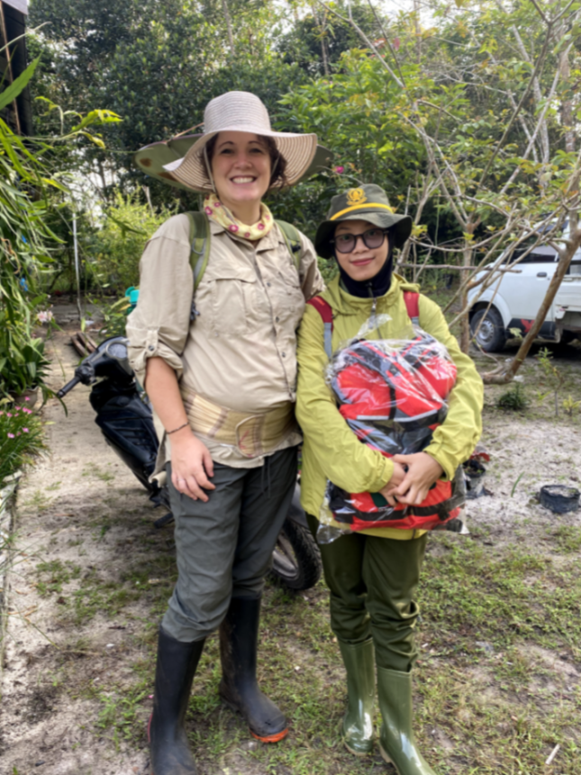 Two people smiling at the camera and holding bags. they are wearing hats and long sleeve clothing