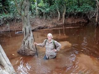 student in the forest waist-deep in water smiling at the camera