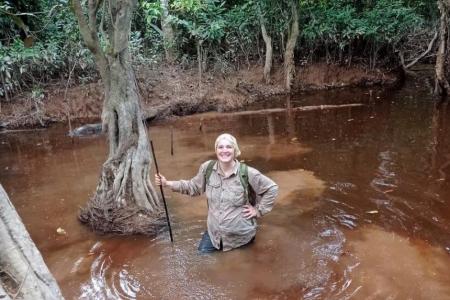 student in the forest waist-deep in water smiling at the camera